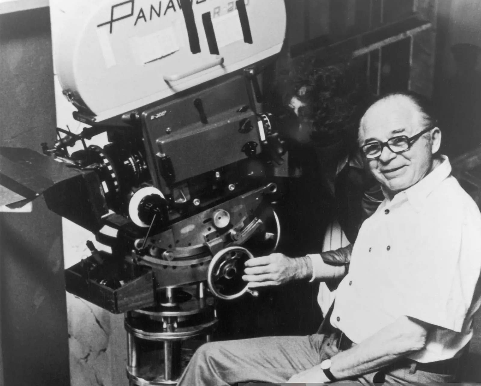 circa 1965: Austrian-Hungarian-born director Billy Wilder (1906 – 2002) smiles while sitting in front of a cameraman on one of his film sets. The cameraman looks through the viewfinder on a Panavision motion picture camera. (Photo by Hulton Archive/Getty Images)